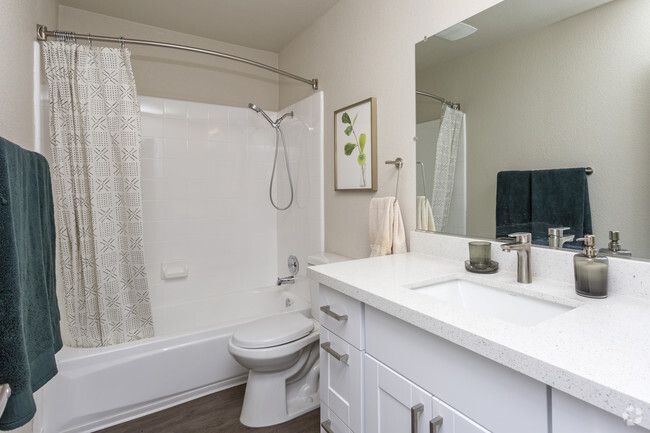 Bright white bathroom with tub-shower, toilet, vanity, and teal towels
