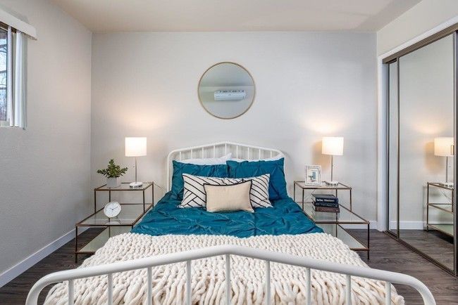 Bright bedroom with white bed frame, teal bedding, mirrored closet, and two bedside lamps