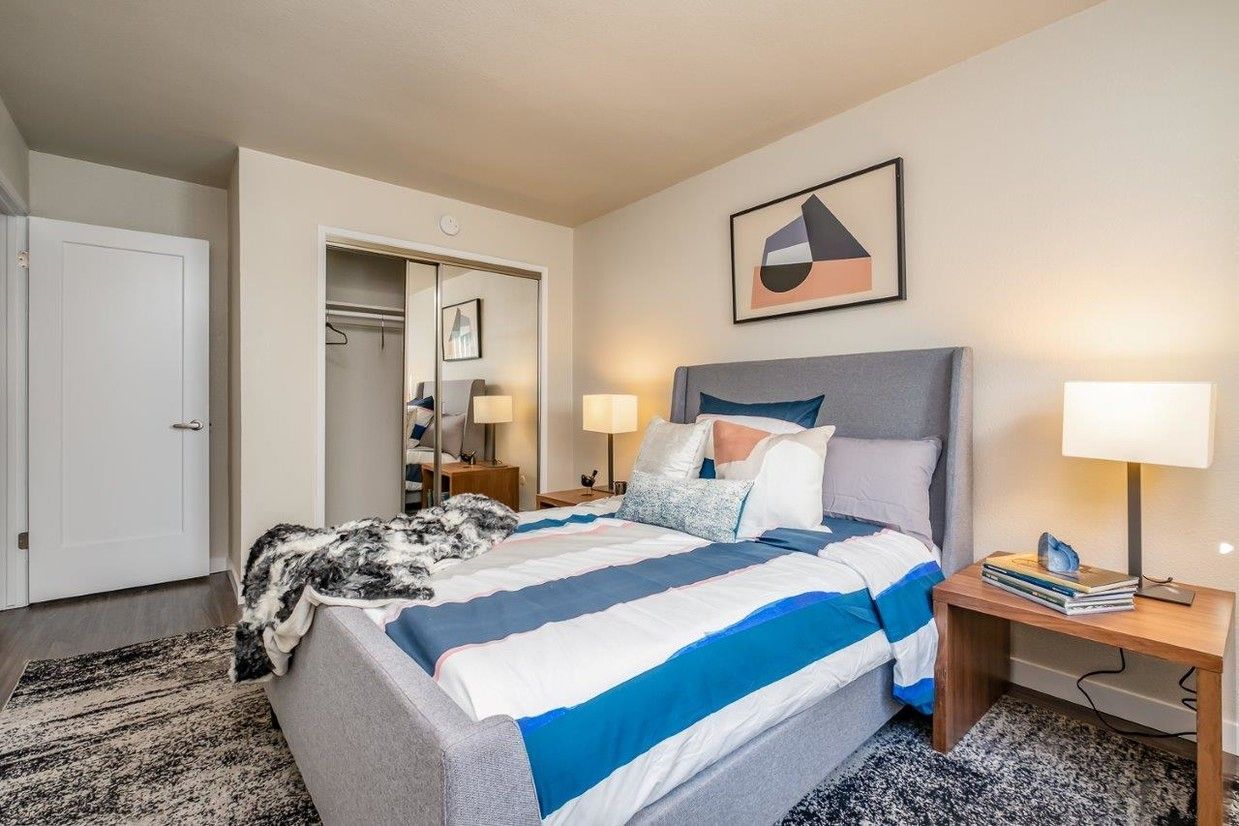Bright bedroom with a bed, two bedside lamps, white closet, and gray carpet