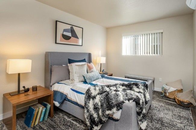 Cozy bedroom with a gray bed, blue accents, lamps, framed art, and a window with blinds