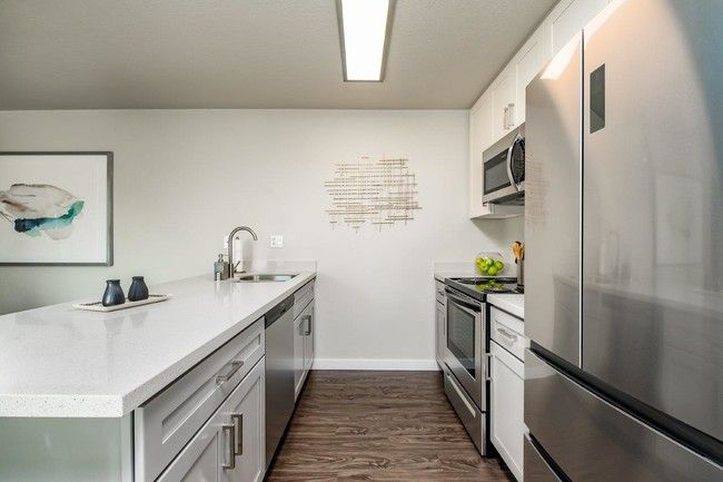 Modern kitchen with stainless steel appliances, white counters, and wood floors