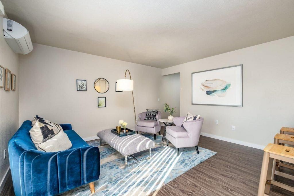 Bright living room with blue velvet chair, patterned rug, coffee table, and wall art in neutral tones