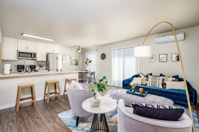 Bright open-plan living room with white kitchen, wood floors, blue sofa, and round dining table