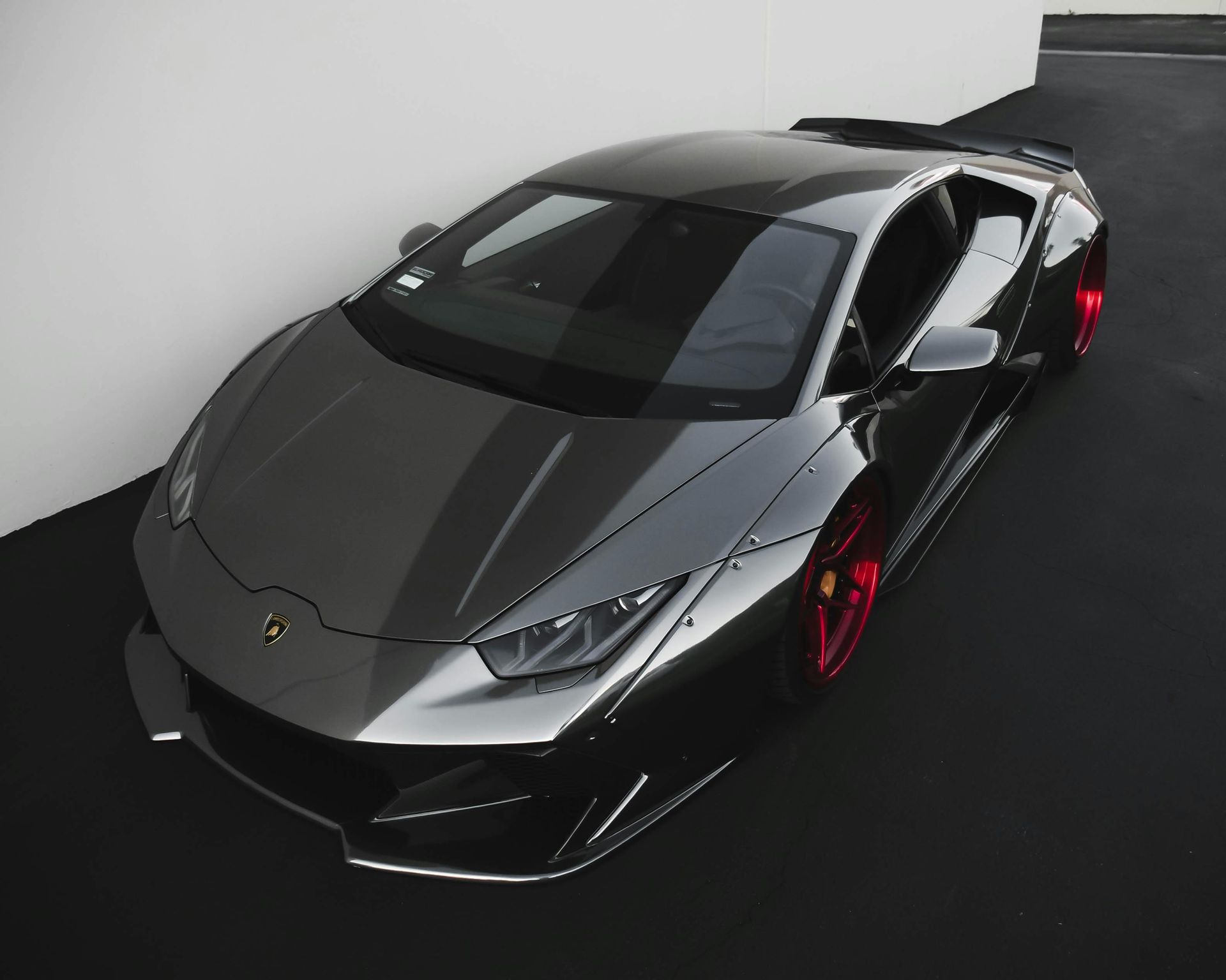 Dark gray Lamborghini with red wheels parked outdoors.