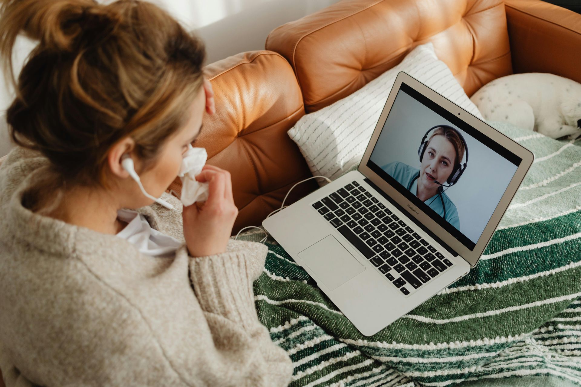 Woman on couch in face mask on a video call with a laptop and phone nearby Woman on couch in face mask on a video call with a laptop and phone nearby
