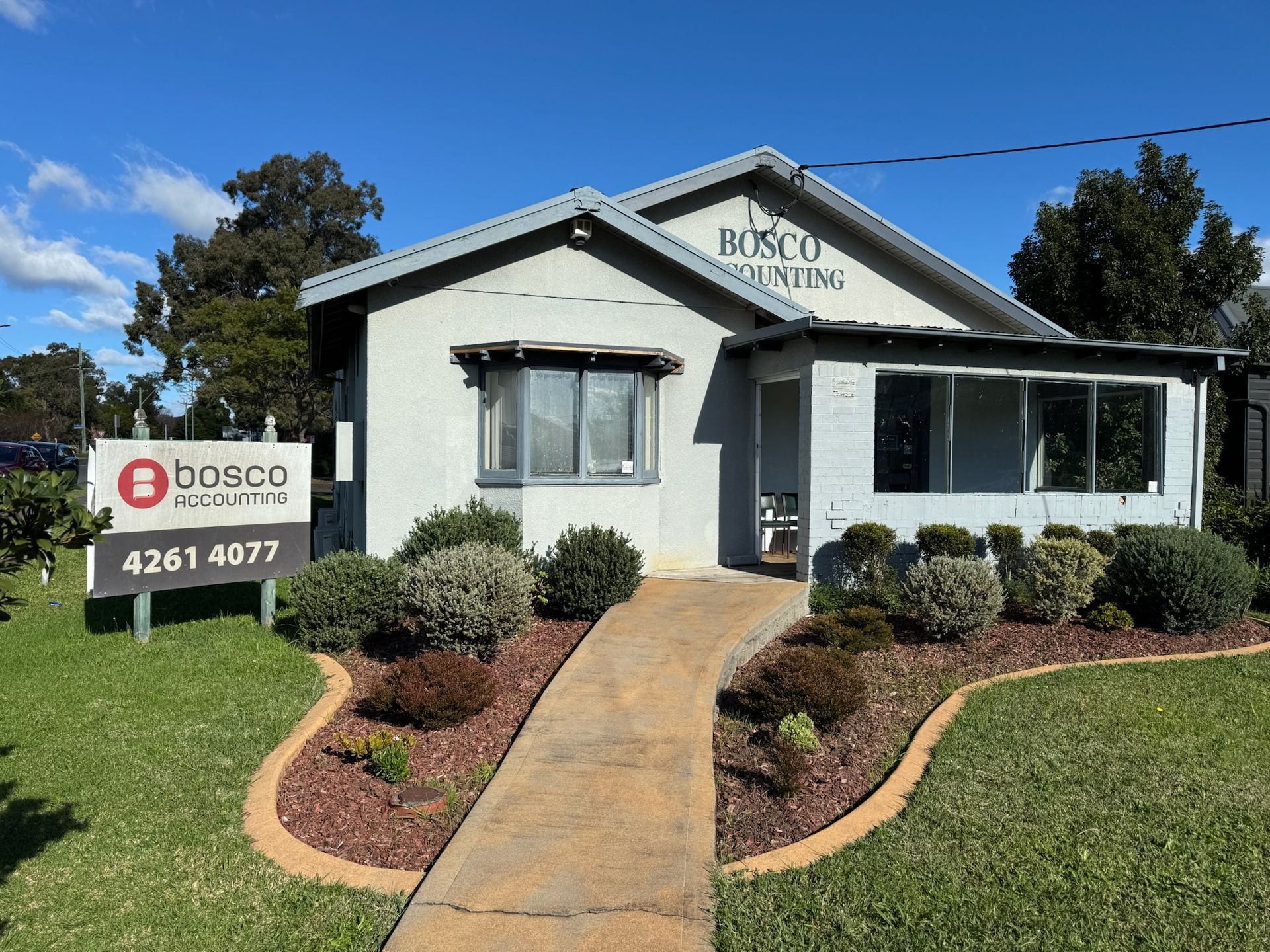 Real estate sign outside a small white house with a curved walkway and landscaped yard - Bosco Accounting Dapto NSW 2530