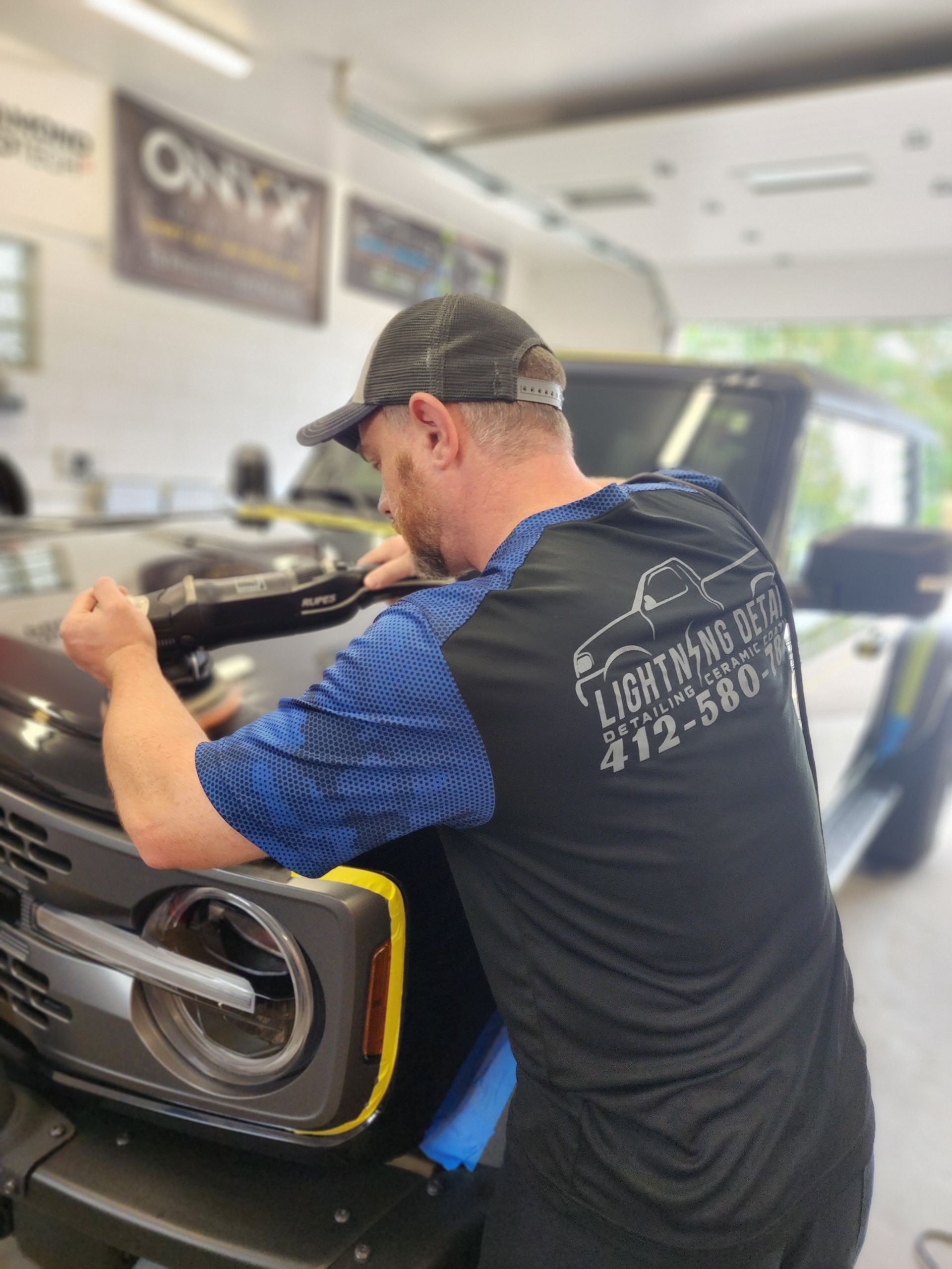 A man is working on the hood of a car in a garage.
