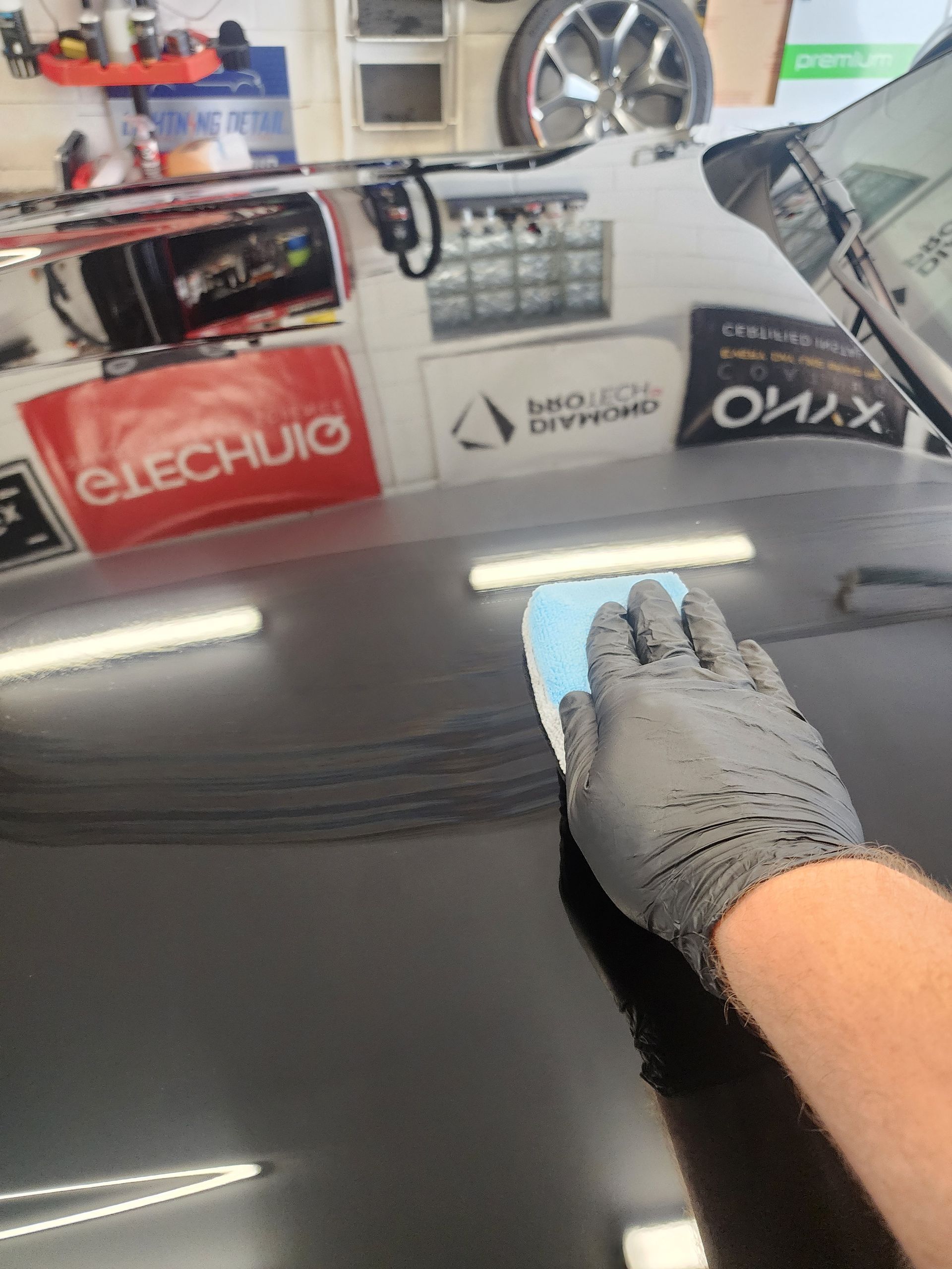 A person wearing a gray glove applies a ceramic coating to a black car's hood.