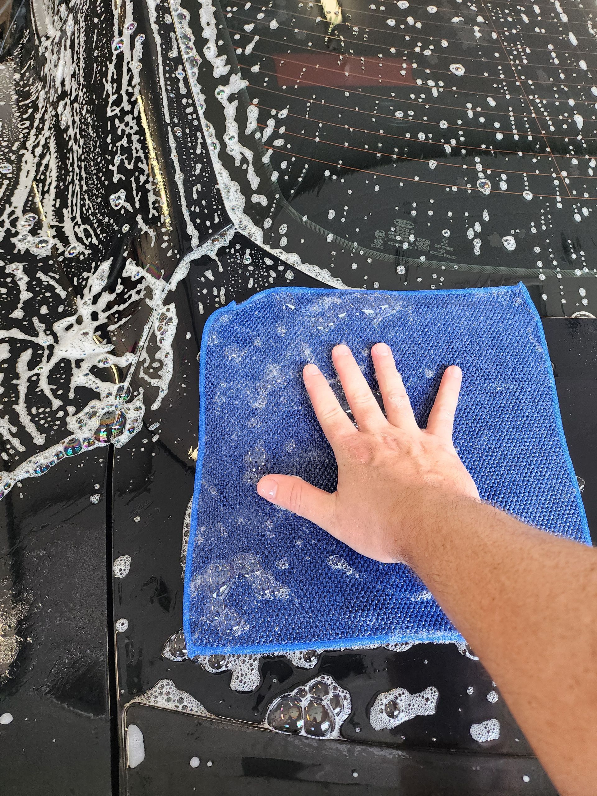 A person is washing a car with a blue towel