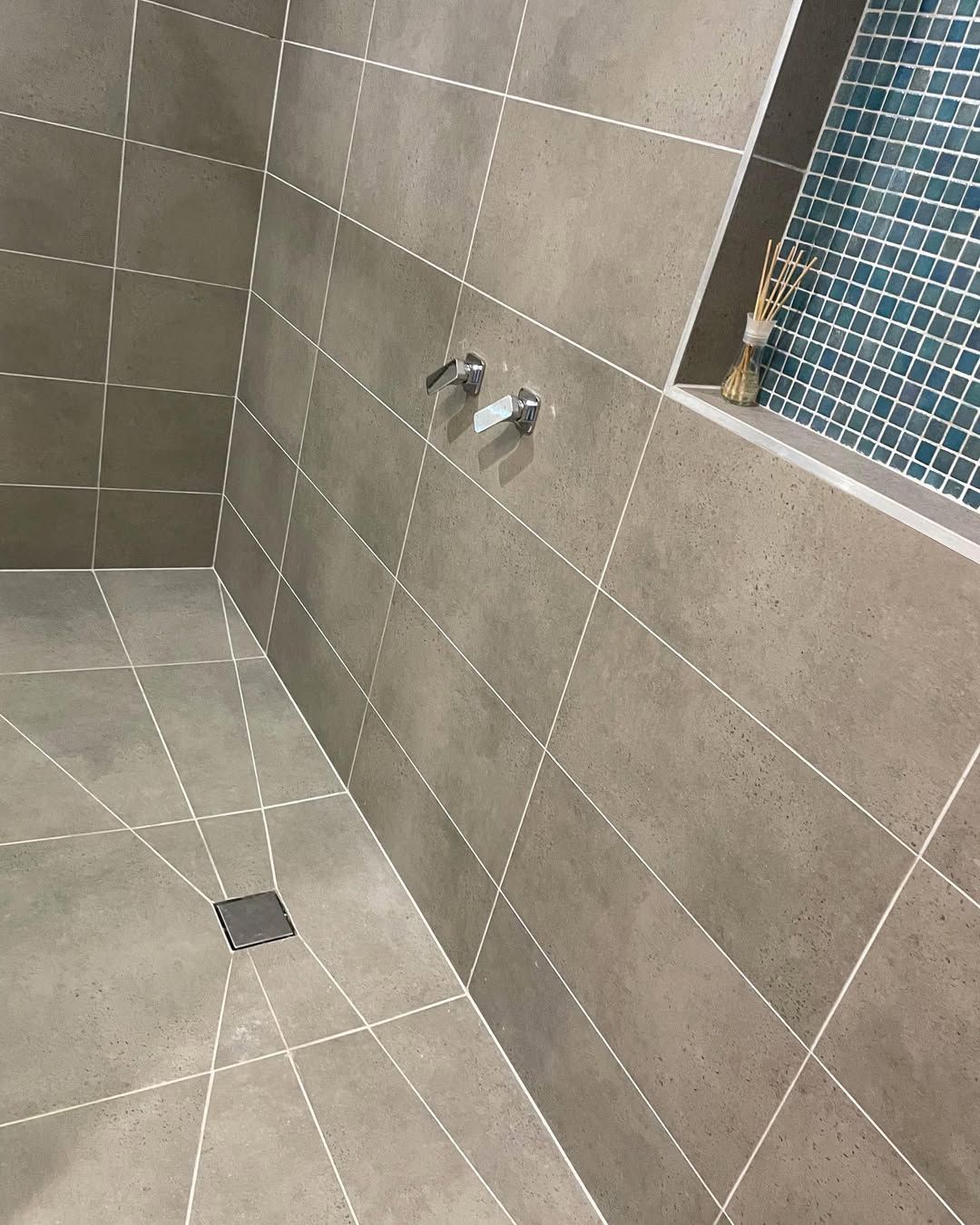 Shower with gray tiles, white grout lines, and a blue mosaic tiled accent wall. — On The Rise Builders in Maroochydore, QLD