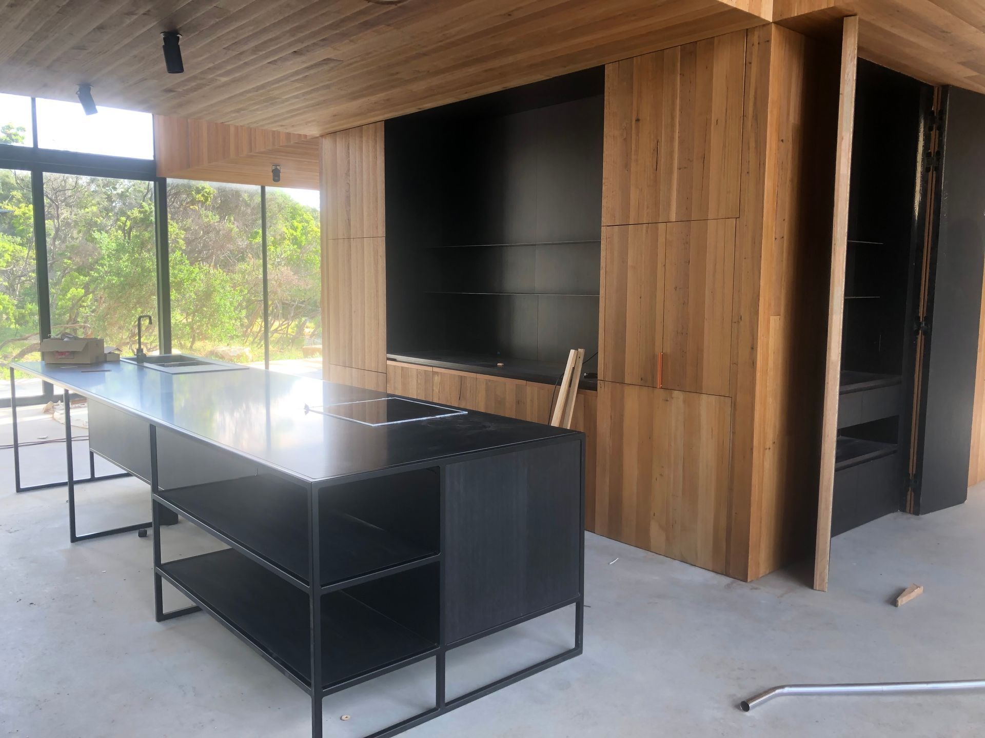 Modern kitchen with black island, light wood paneling, and large windows.— On The Rise Builders in North Arm, QLD