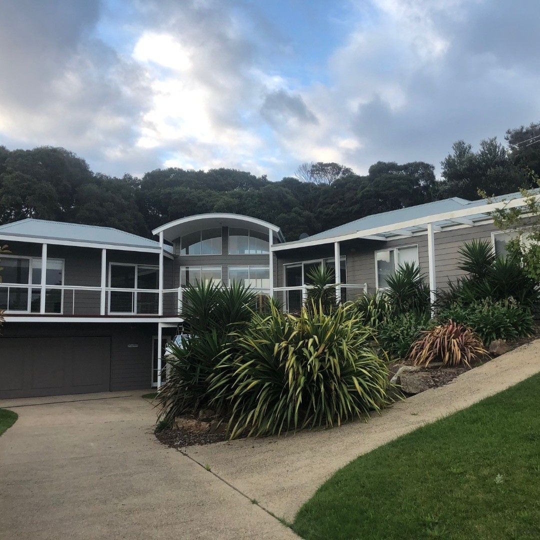 A modern house with a driveway, lush landscaping, and a cloudy sky.