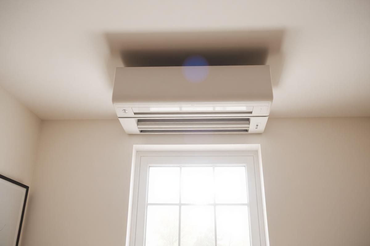Wall-mounted white air conditioner above a window in a beige room