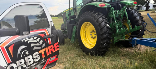 Red Bobst Tire truck parked beside a green tractor with yellow wheels in a grassy field.