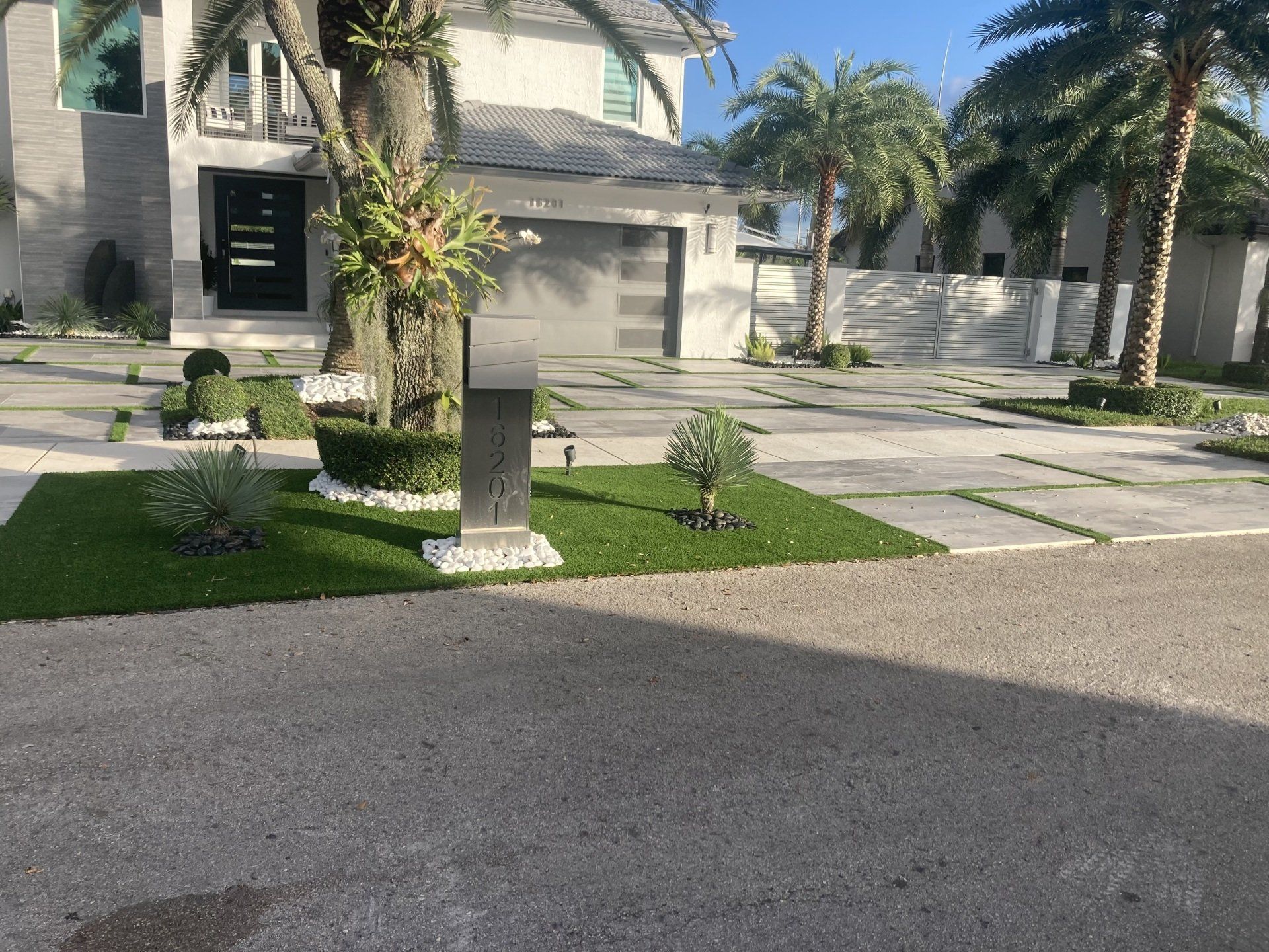 Modern house with palm trees, green grass, and gray driveway. Shiny mailbox in front.