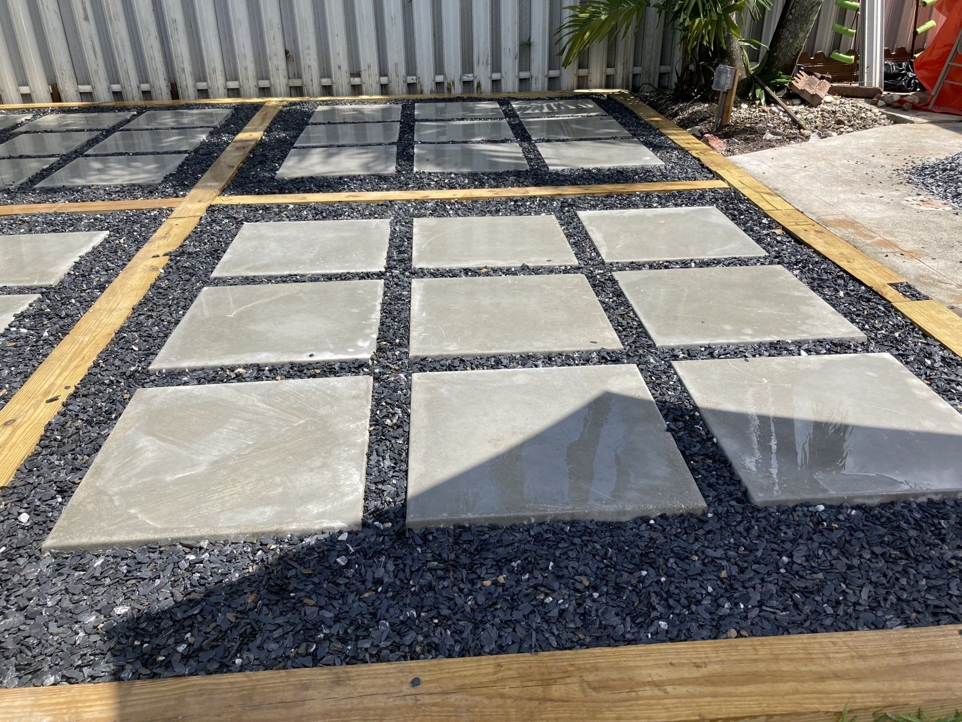 Gray concrete pavers set in black gravel, bordered by wood, in a yard.
