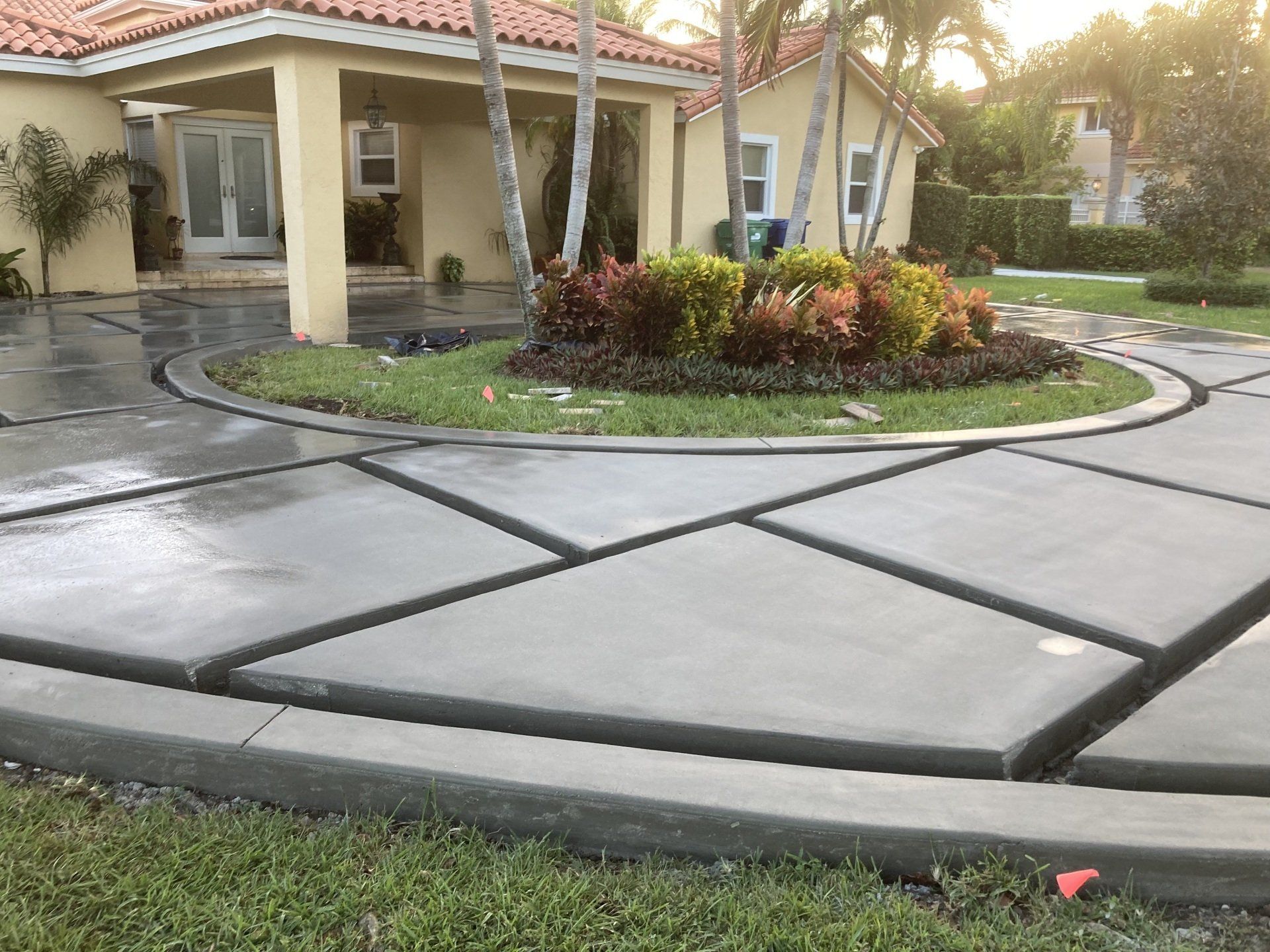 Circular driveway with concrete blocks and a central flowerbed in front of a beige house.