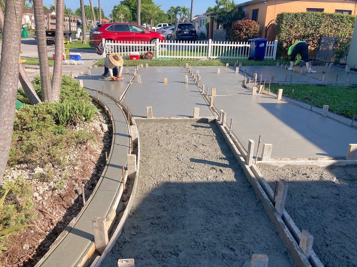 Workers pouring and smoothing fresh concrete for a driveway and walkway in front of houses.