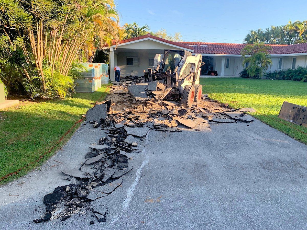 Driveway demolition in front of a house, with an excavator tearing up the asphalt.