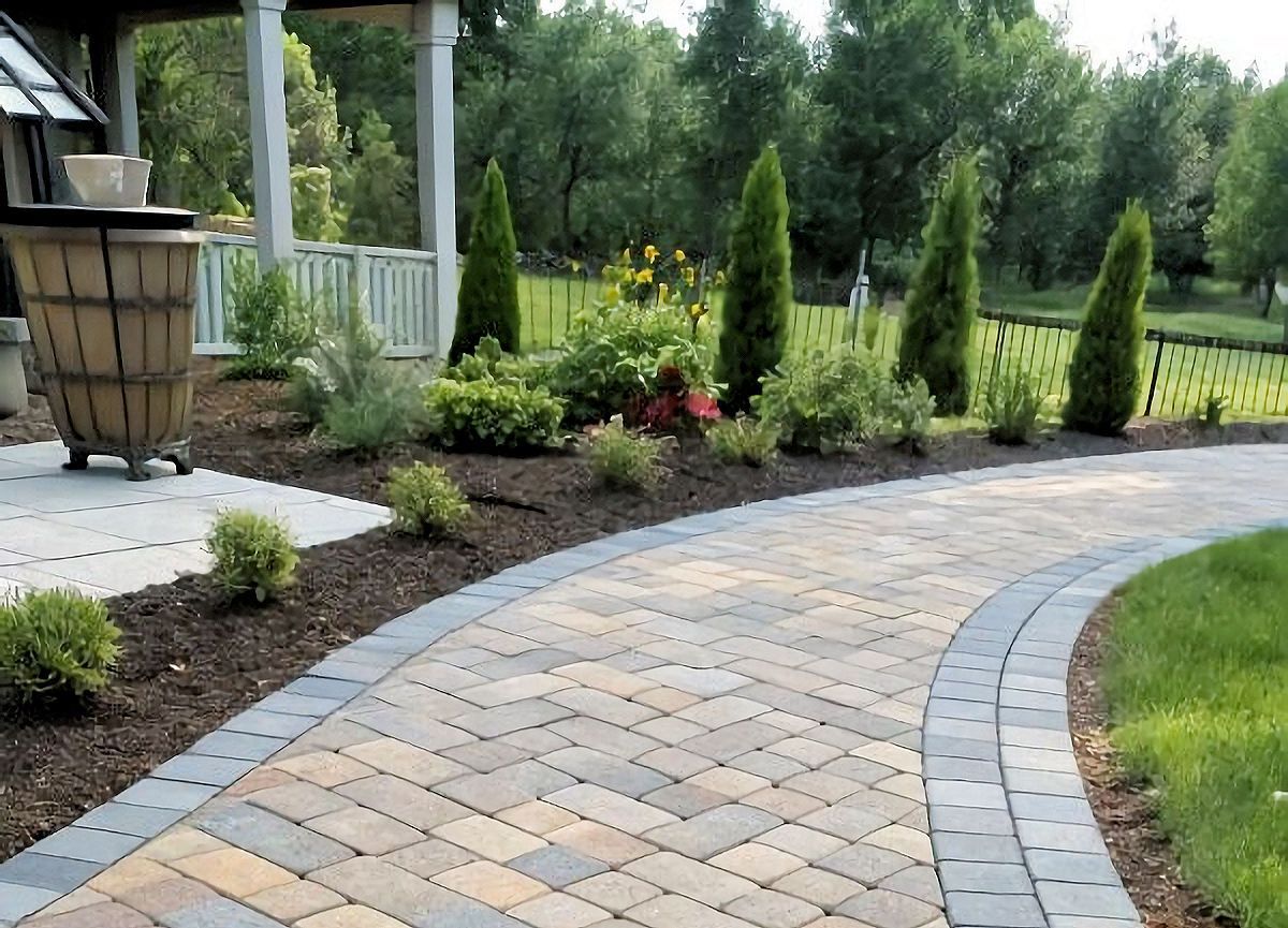 Curving brick path bordered by dark gray bricks and mulch, leading through a landscaped garden.