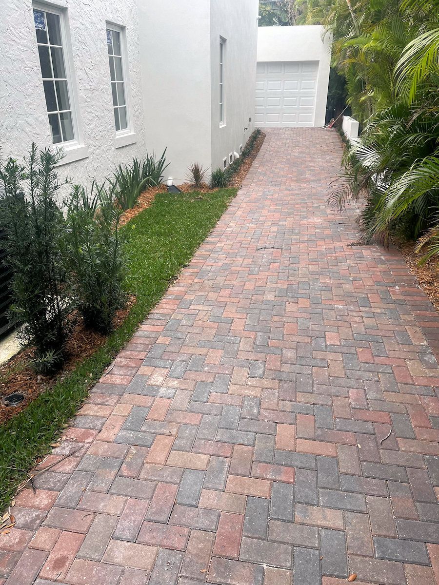 Brick driveway leading to a garage next to a white building with landscaping.