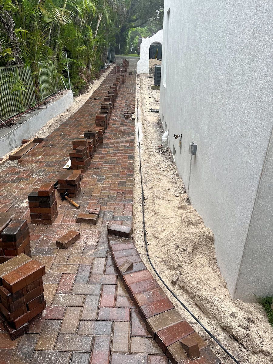 Brick pathway construction in progress, alongside a building with a white exterior.