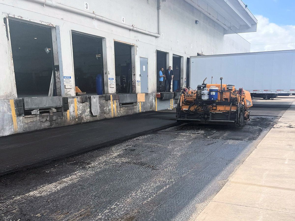 Asphalt paving machine laying new pavement at a loading dock.