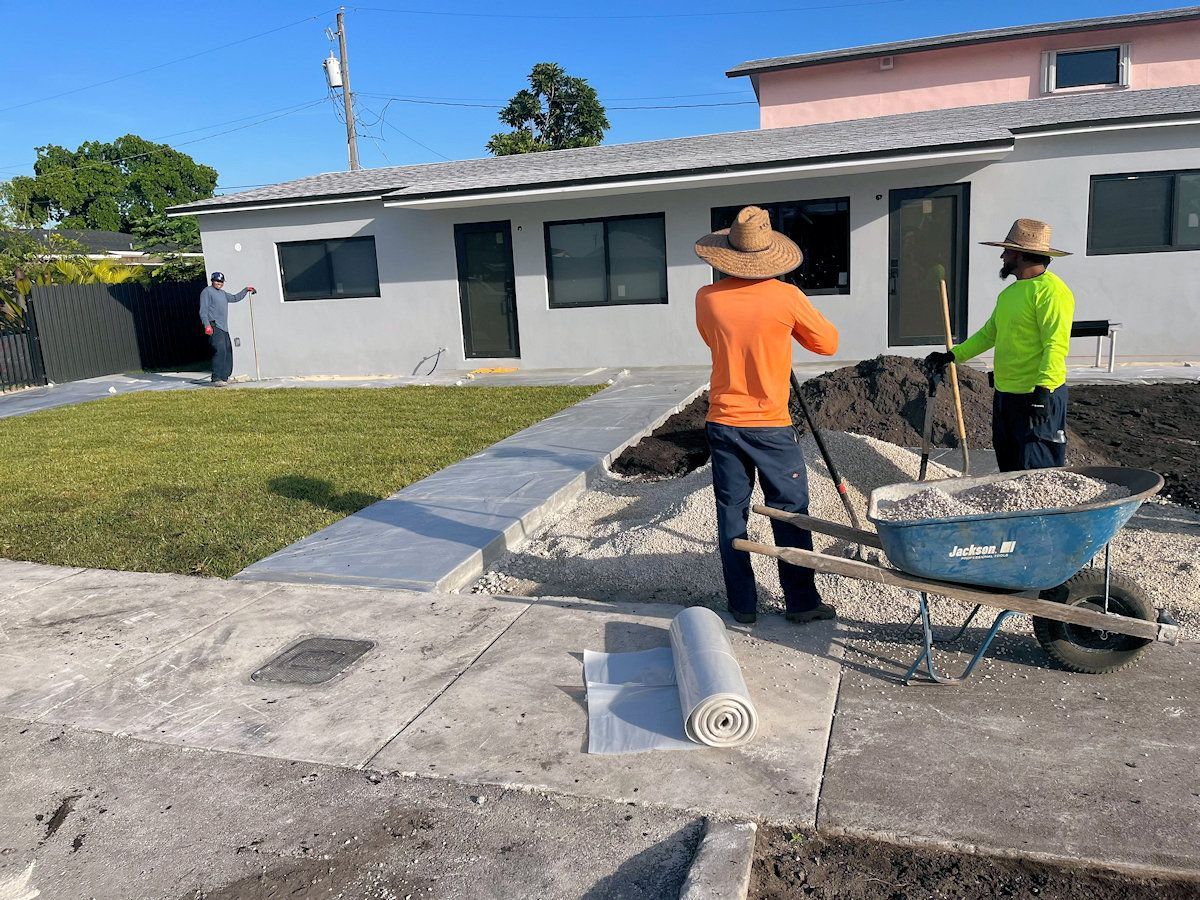 Construction workers landscaping a home's front yard; one using a wheelbarrow, one with a shovel, one gesturing.