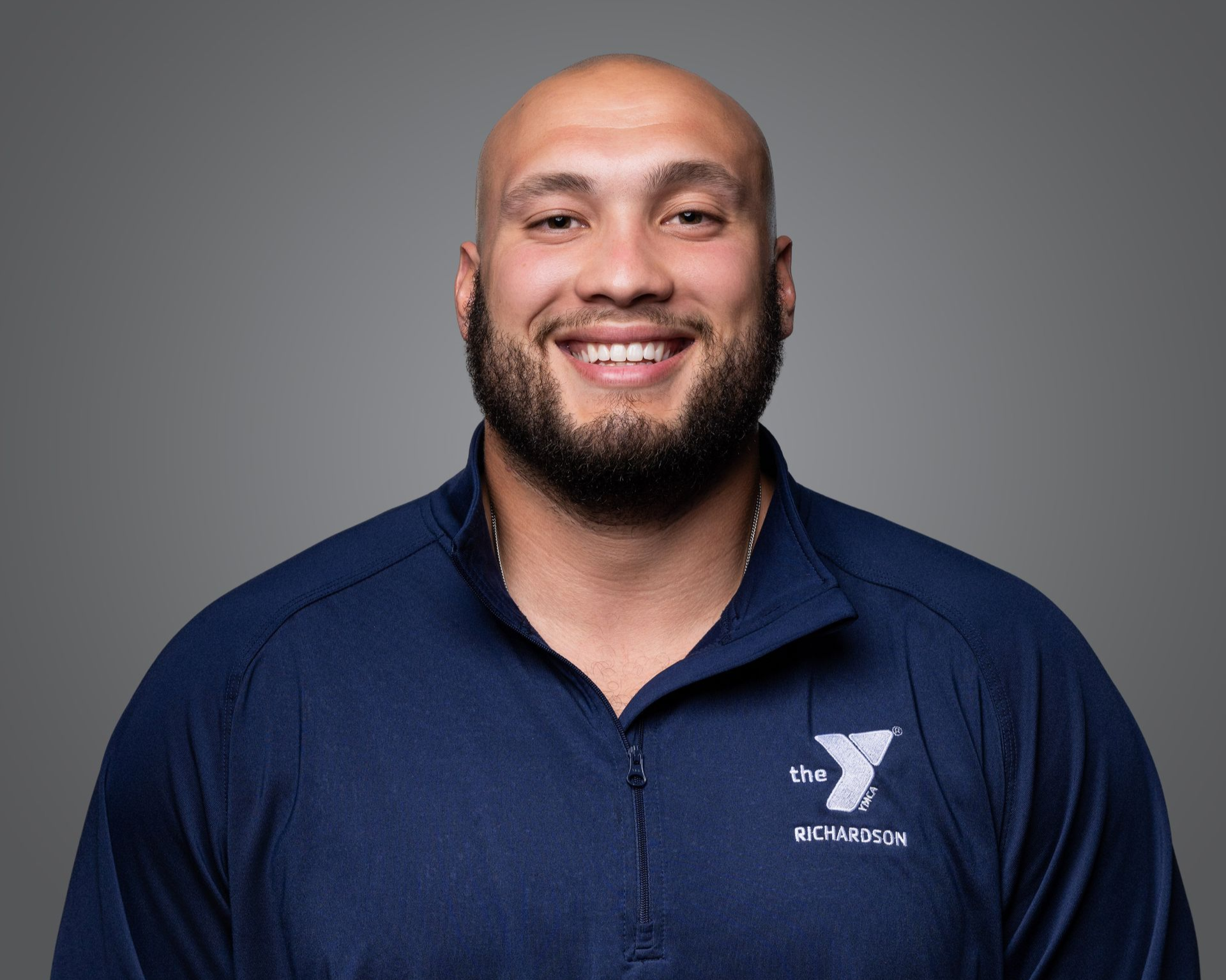 Smiling bald man in navy polo shirt against a gray studio background