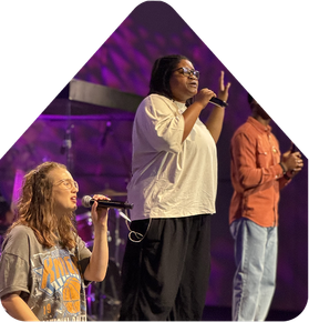 Three singers perform onstage under purple lighting, each holding a microphone.