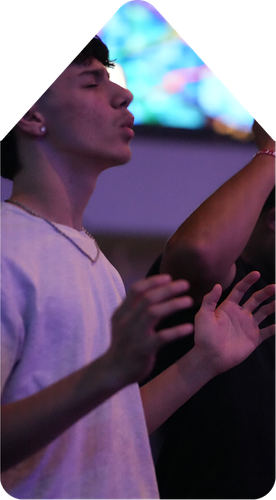 Person singing with eyes closed at a purple-lit event, hands raised in the foreground
