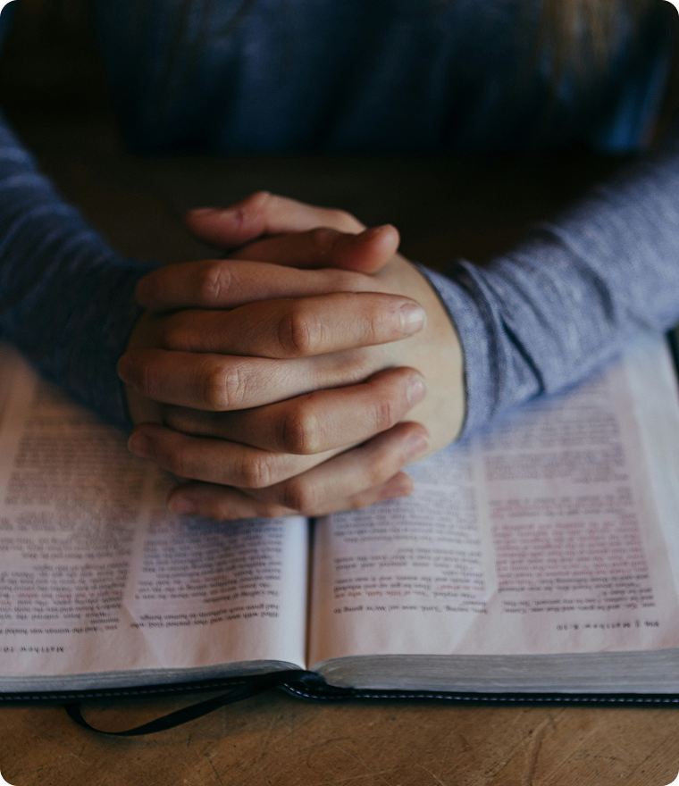 Hands clasped in prayer over an open Bible.