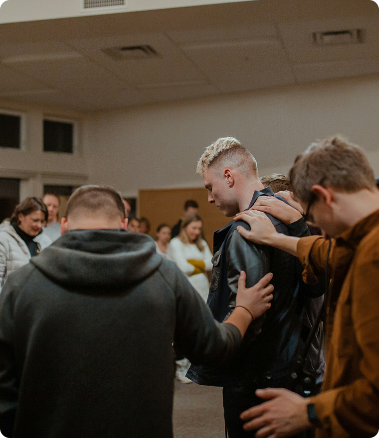 People in a room praying together, with hands on one another’s shoulders.