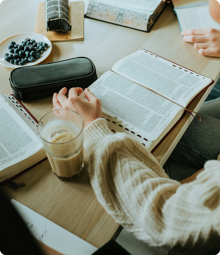 People reading books at a wooden table with coffee, pencils, and a pencil case