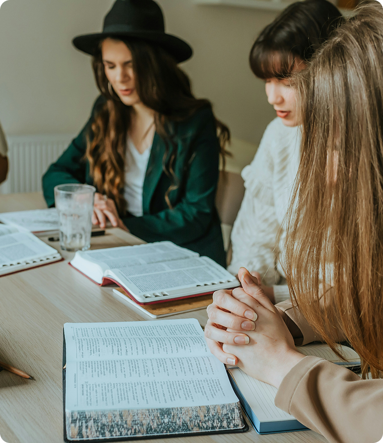 Three people reading and writing at a table with open books in a bright room