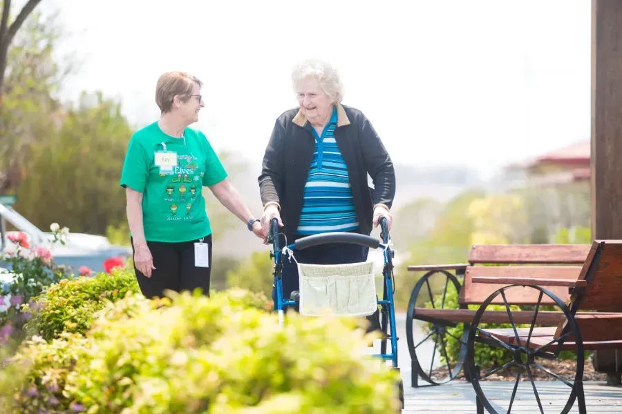 A nurse at Beauaraba Living is helping an elderly woman with a walker.