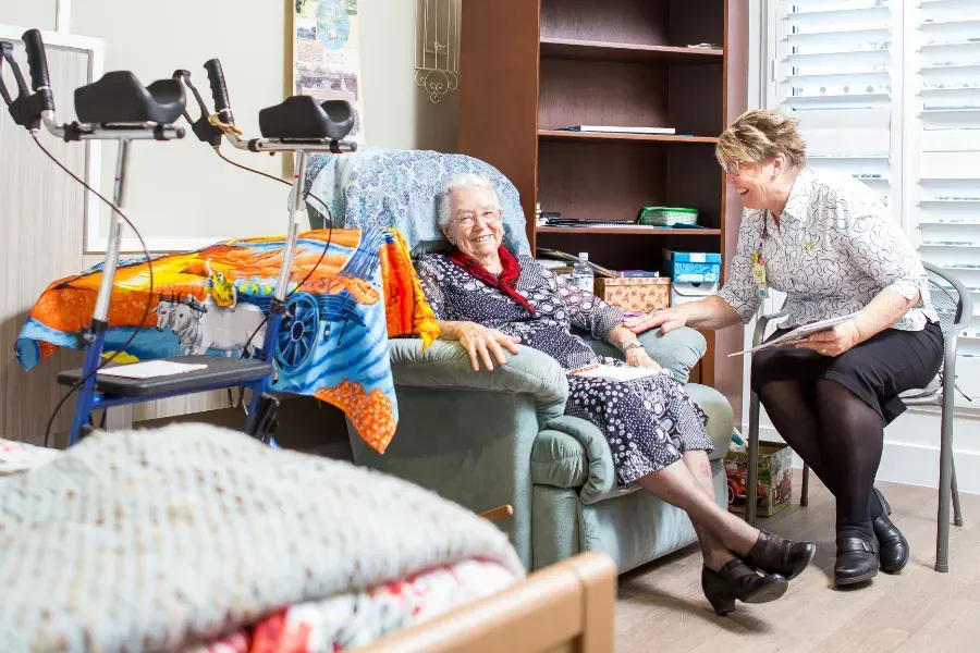 A woman is sitting on a chair next to an elderly woman in a room at Beauaraba Living.