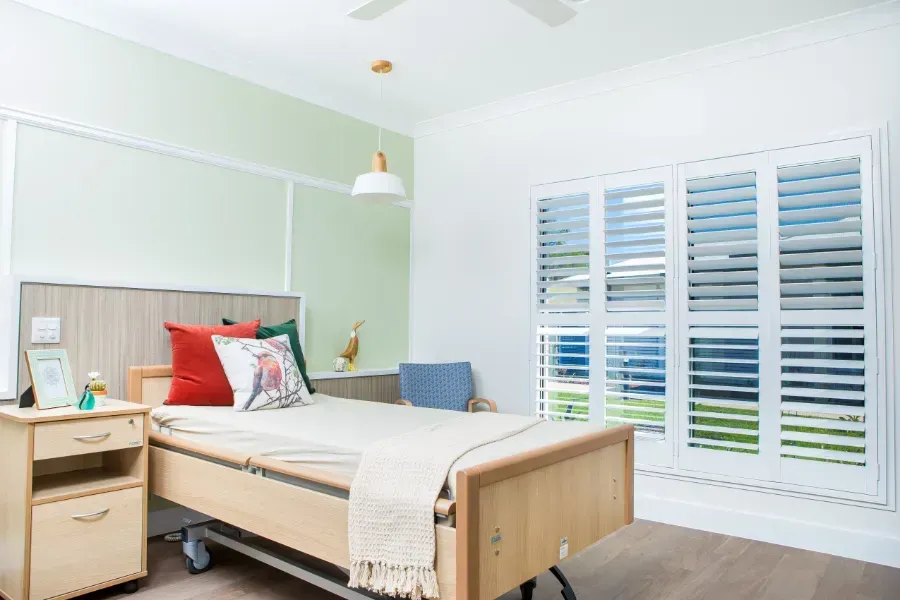 A single bed room at Beauaraba Living with a nightstand and shutters.