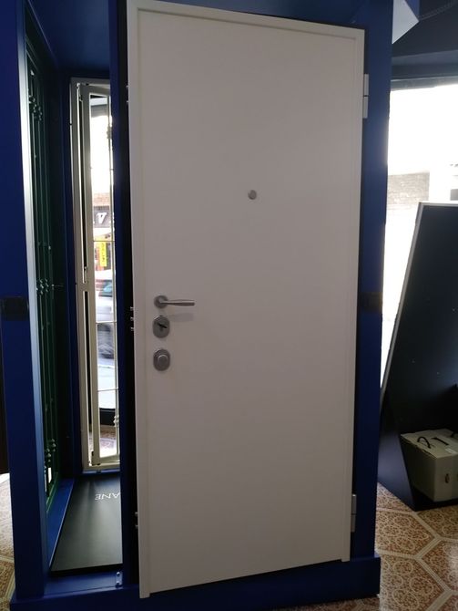 Porta di sicurezza bianca con spioncino, maniglia a leva e catenaccio in una cornice blu.