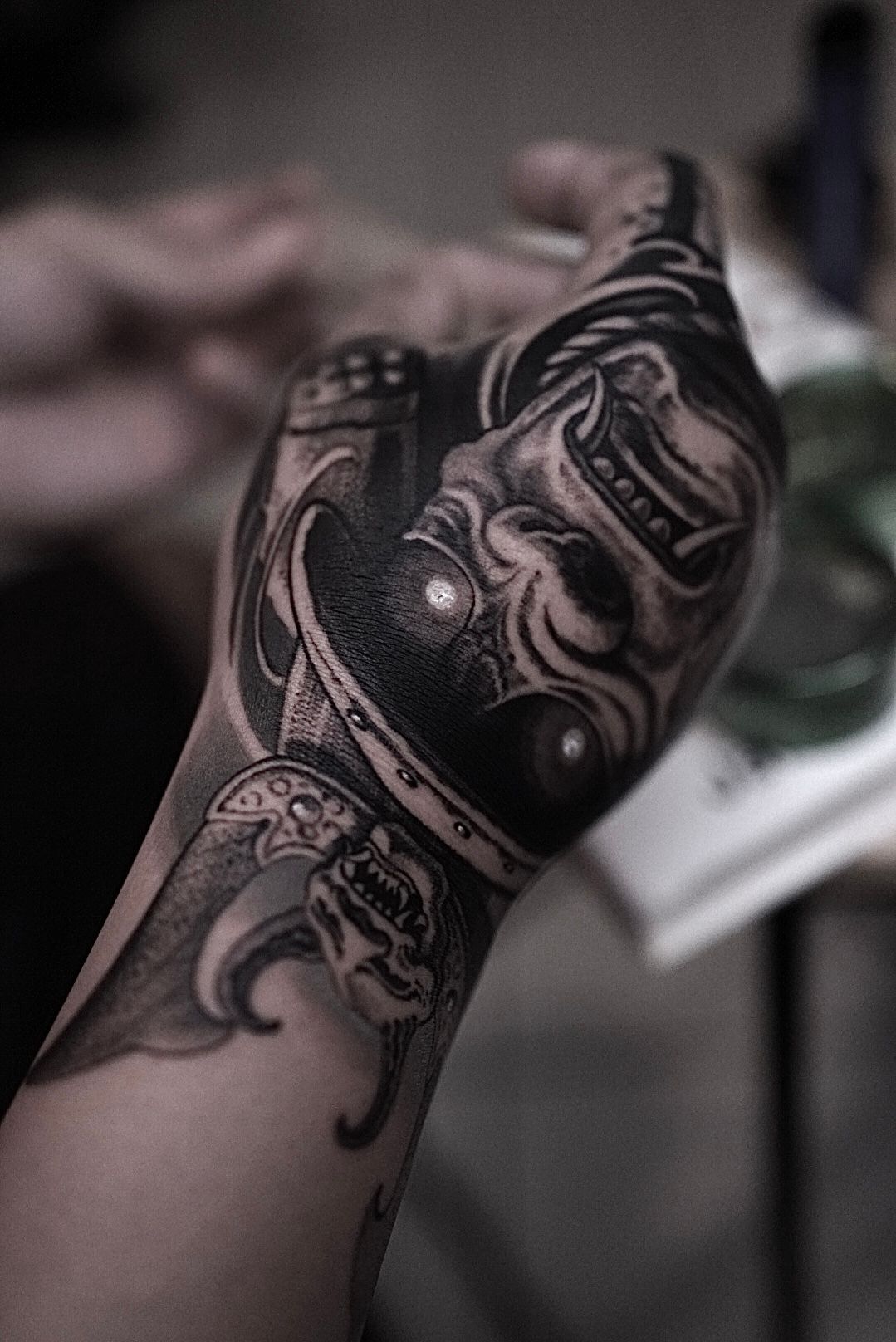 Hand tattoo featuring a samurai helmet and a curved sword, rendered in grayscale. Hand tattoo