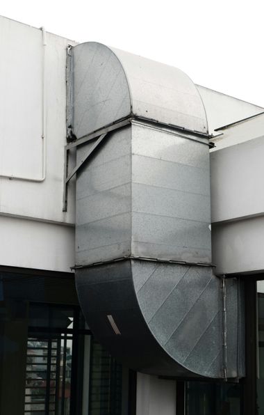 Large silver ventilation duct on a building exterior beneath a white overhang