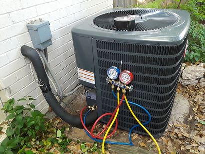 Outdoor air conditioner unit with exposed gauges and colored hoses beside a brick wall