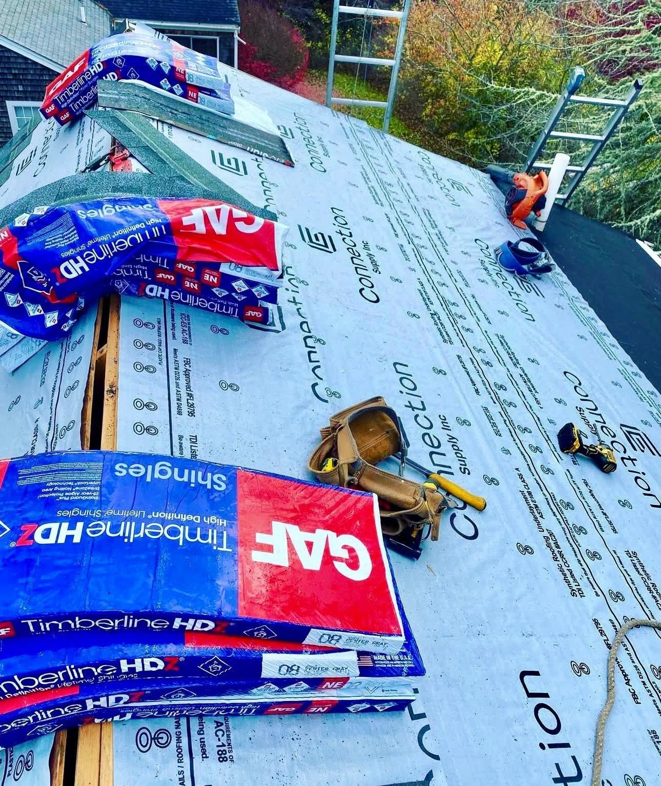 Roof under construction with blue and red GAF shingles, tools, and roofing materials spread out.
