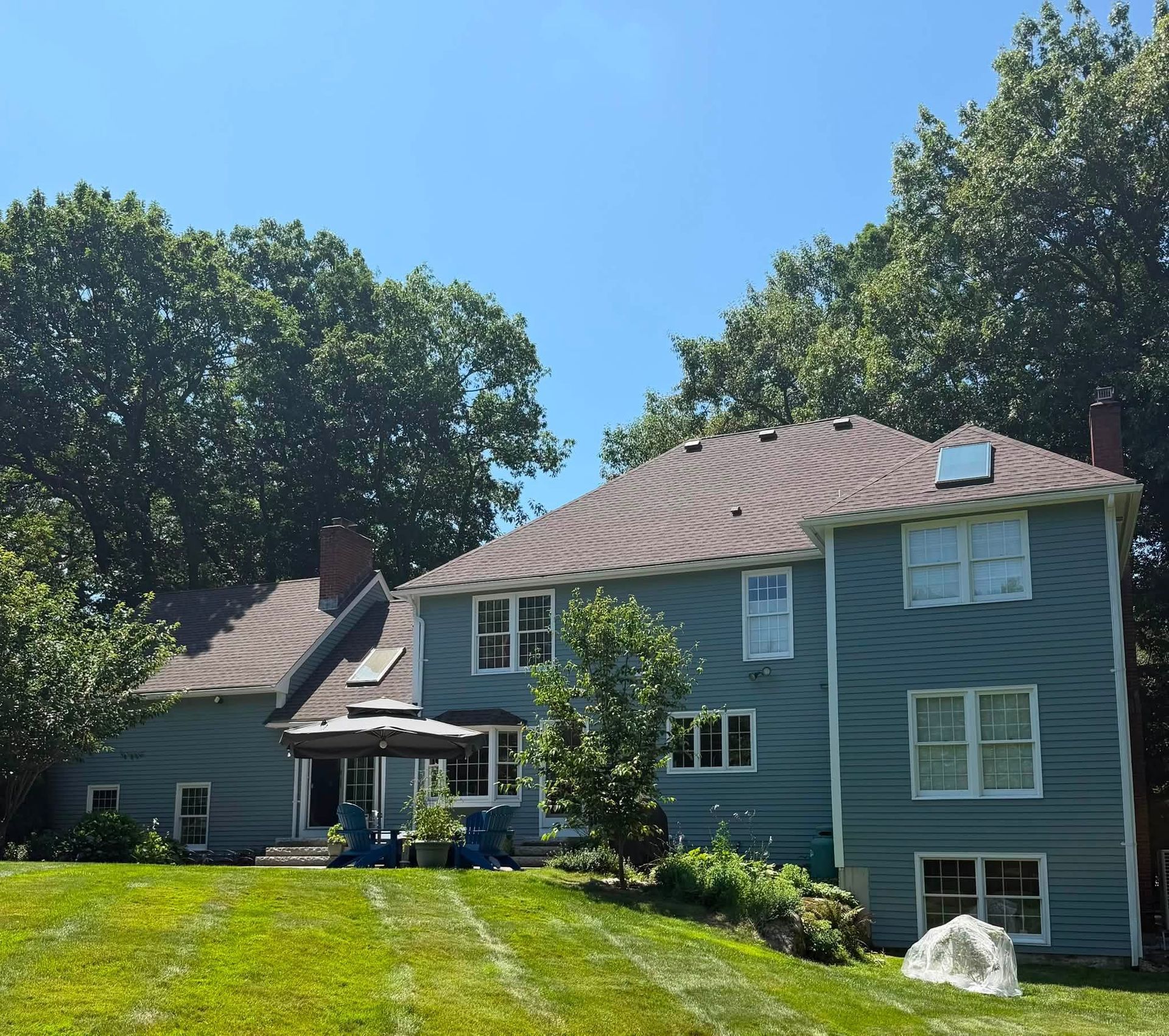 Blue two-story house with white-trimmed windows, red roof, and green lawn under a sunny sky