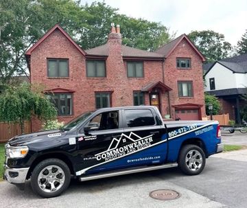 Black pickup truck with blue graphics parked in front of a red brick house.