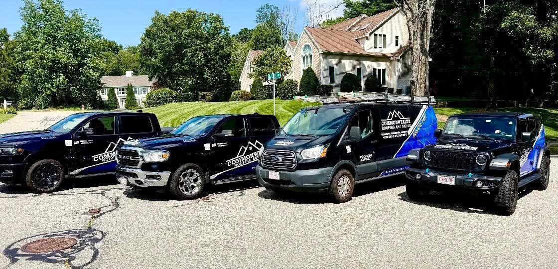 Four black SUVs and a blue sports car parked on gravel in front of a house