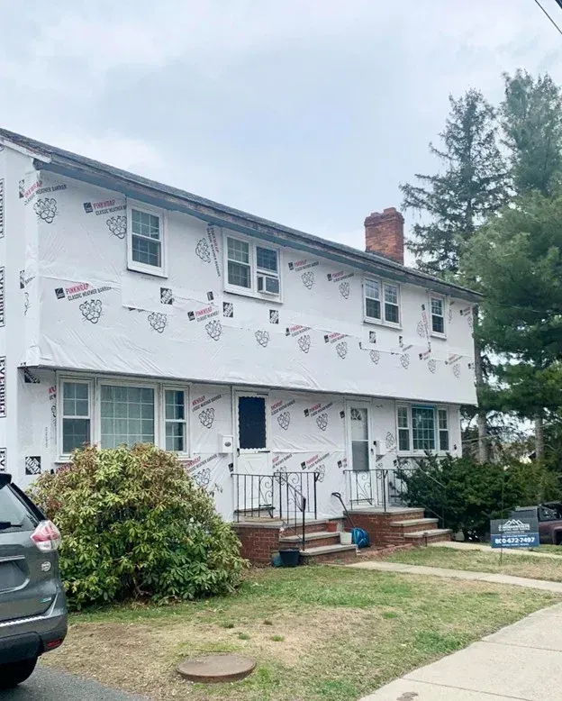 Two-story white apartment building with pennant banners, front steps, and parked cars under an overcast sky