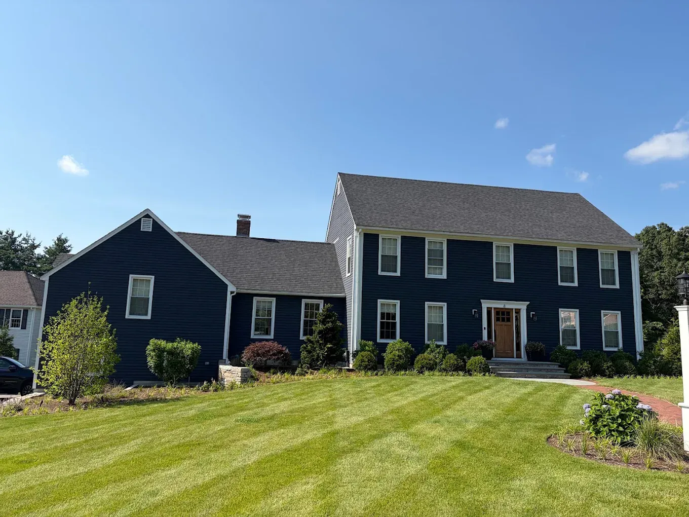 Dark blue two-story house with a striped green lawn under a clear blue sky
