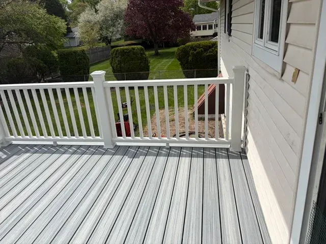 White deck with railing overlooking a green backyard and steps leading down to the lawn