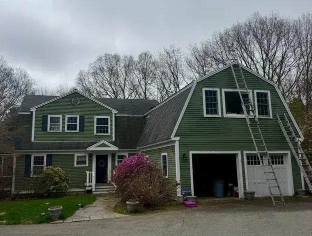 Green two-story house with attached garage, white trim, and pink flowering bush in front yard